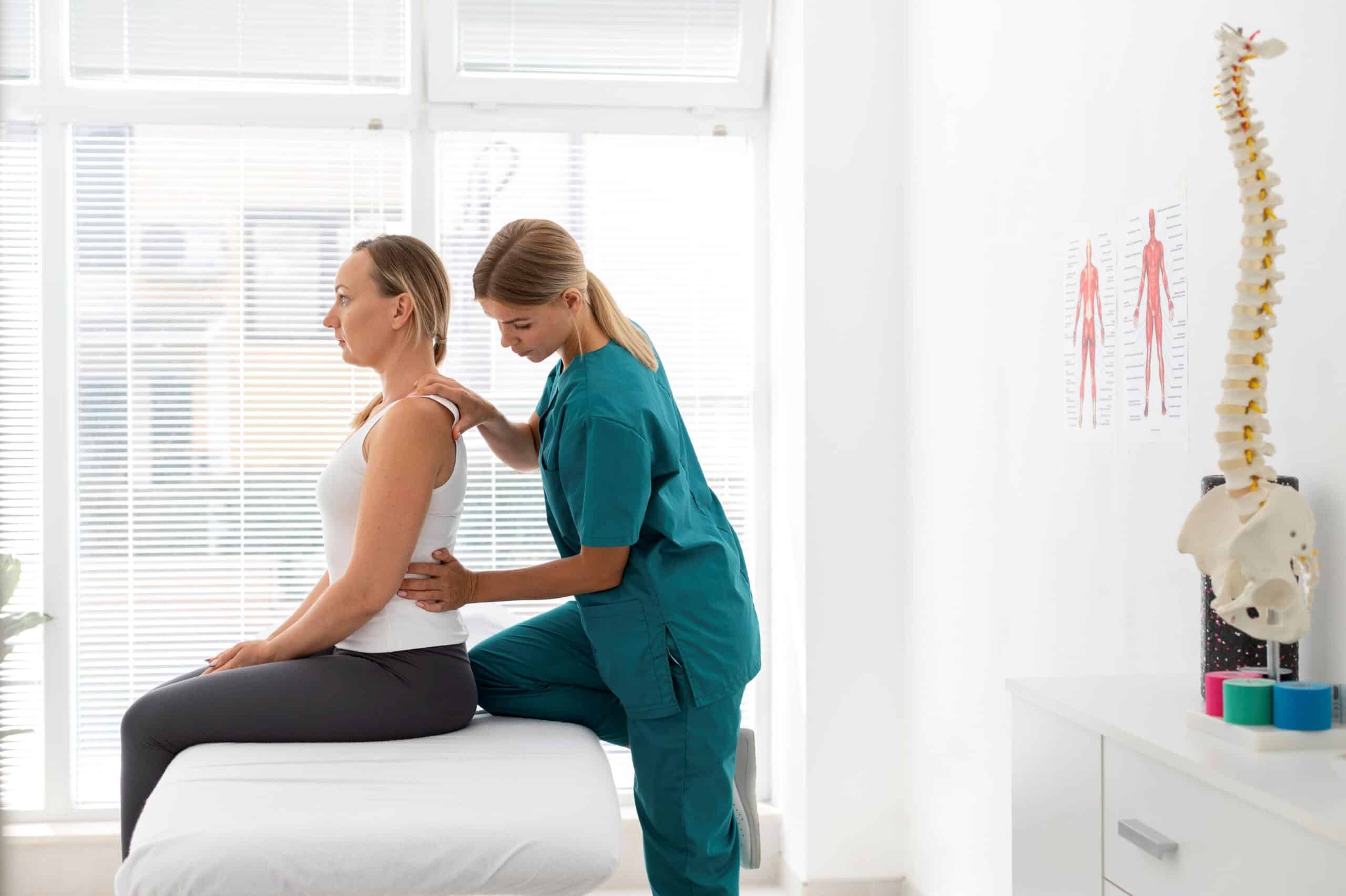 Can Adhesions Cause Back Pain, image of a woman patient sitting upright on a doctor’s table while a physical therapist grasps her back.