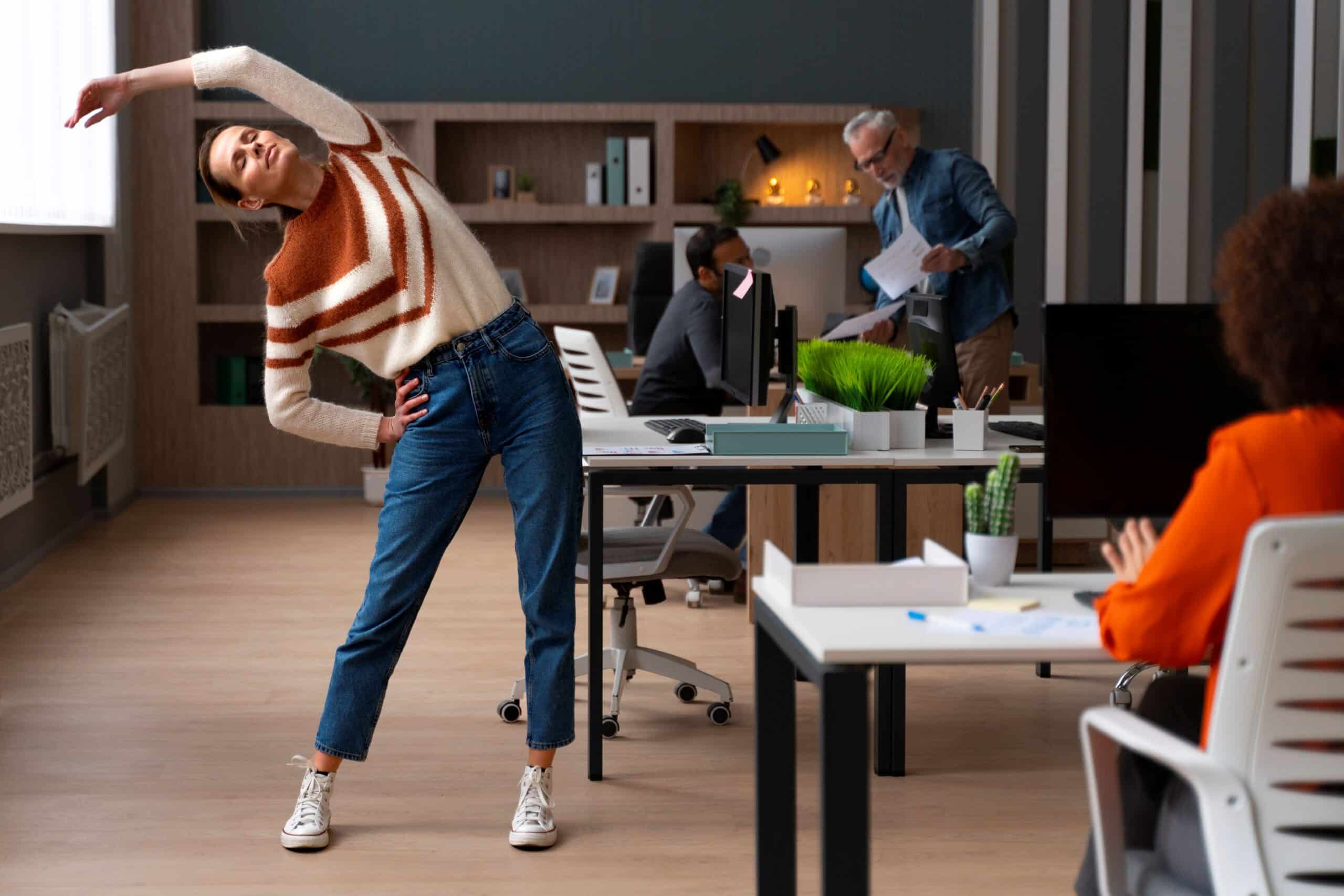 Back pain from sitting at desk, image of a woman standing and stretching next to her desk.