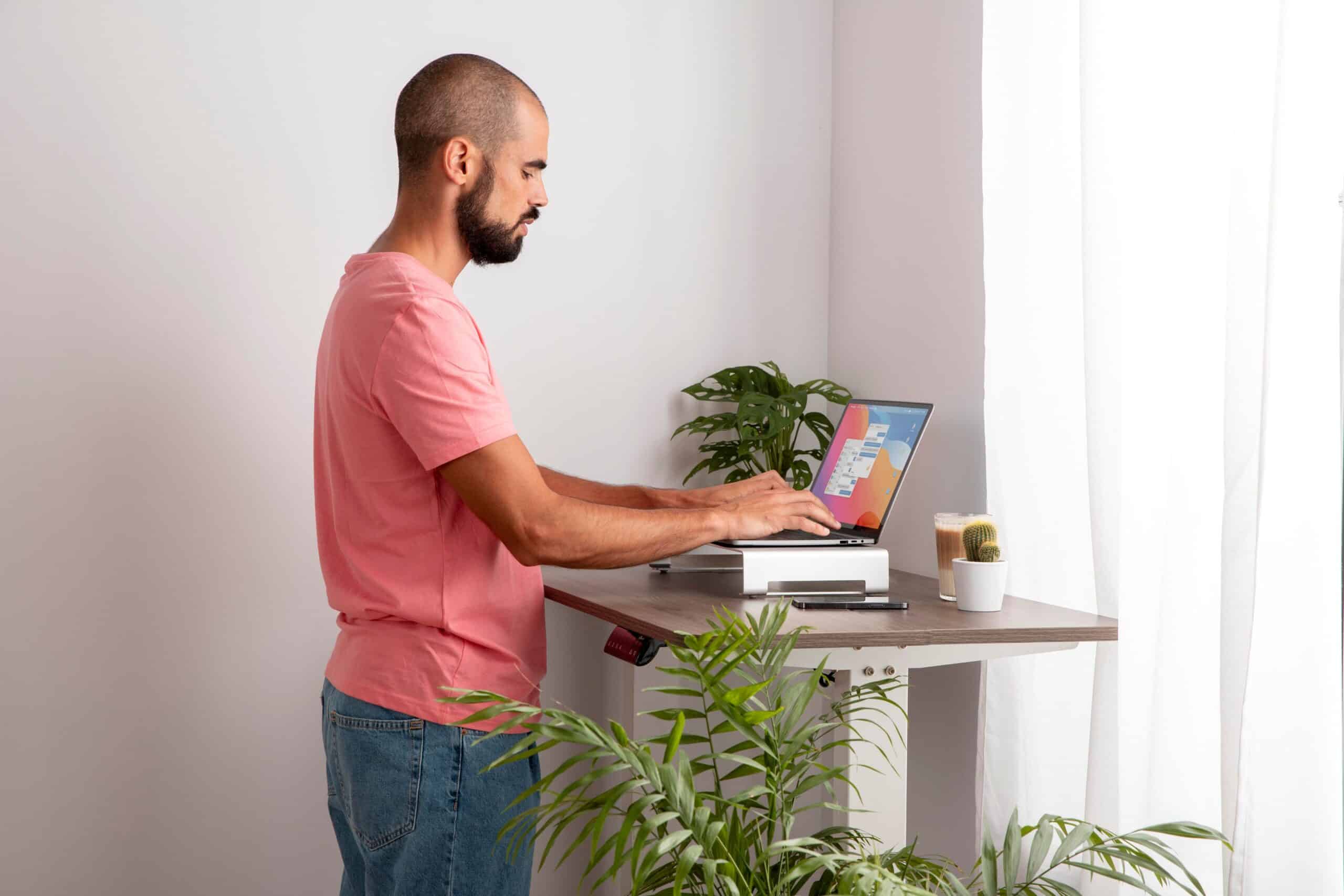 Back pain from sitting at desk, image of a man standing at a desk using his laptop.
