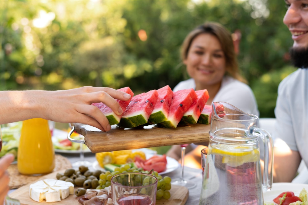 Can Heat Cause Headaches, image of people sitting around a full table outside with a person passing a tray of watermelon slices.