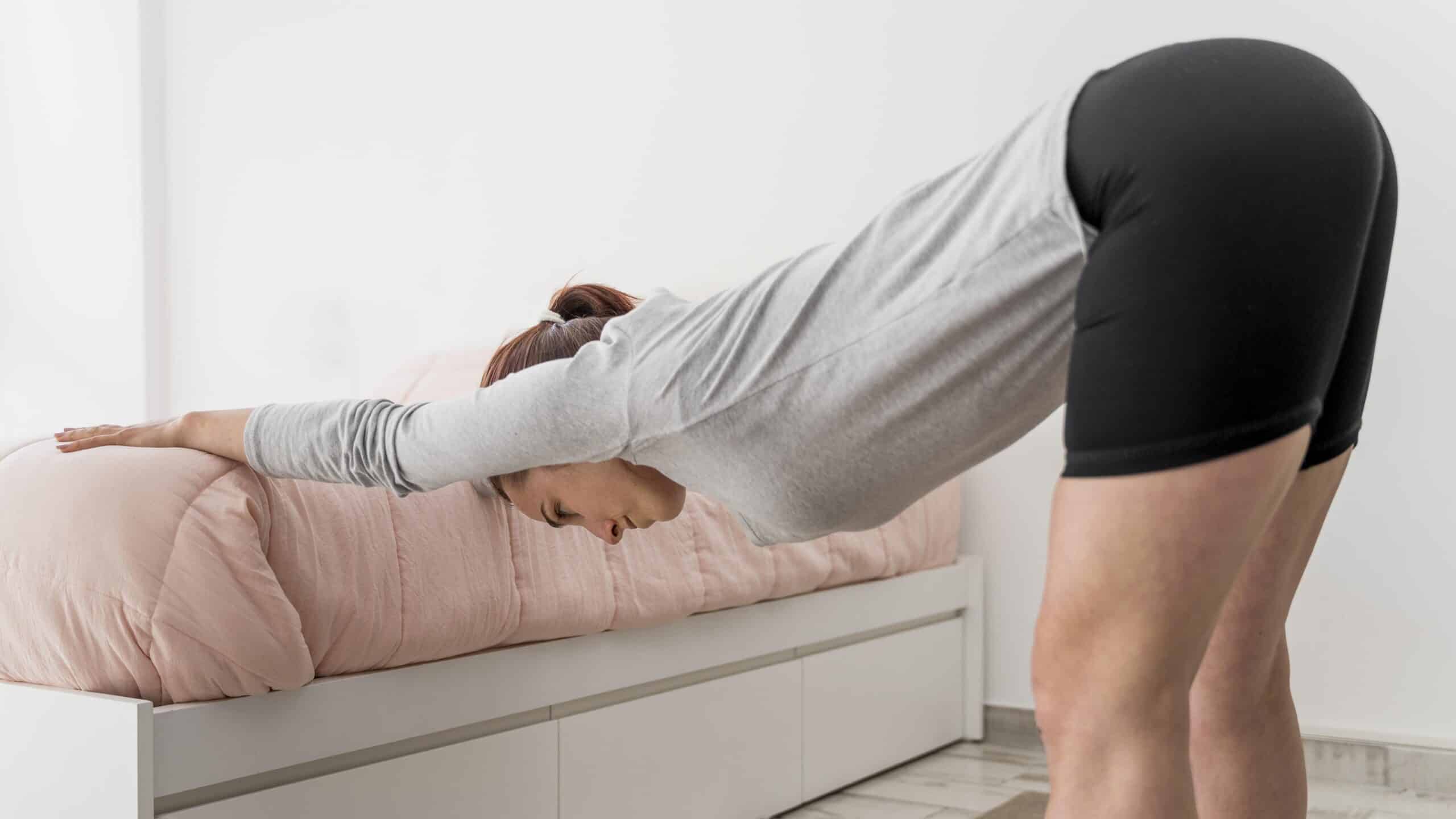 Why does my back hurt when I lie down, image of a woman stretching her back off the right side of a pink bed.