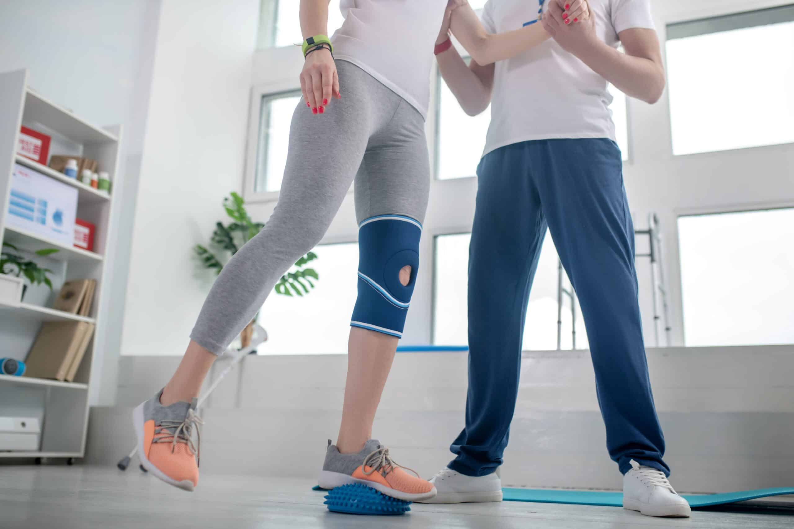 Gait training, image of a male physical therapist helping a female patient balance as she stands on an inflated ball with her left leg.