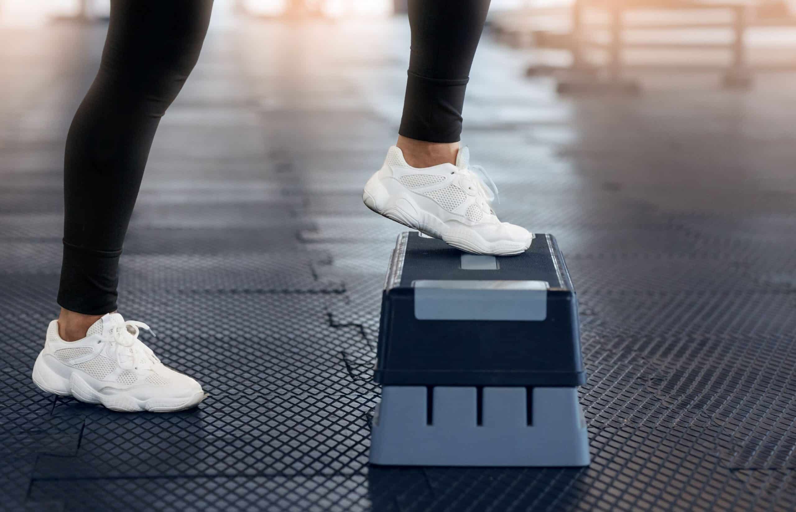 Gait training, image of a woman wearing black workout pants and white sneakers steps up onto a platform with her left leg.