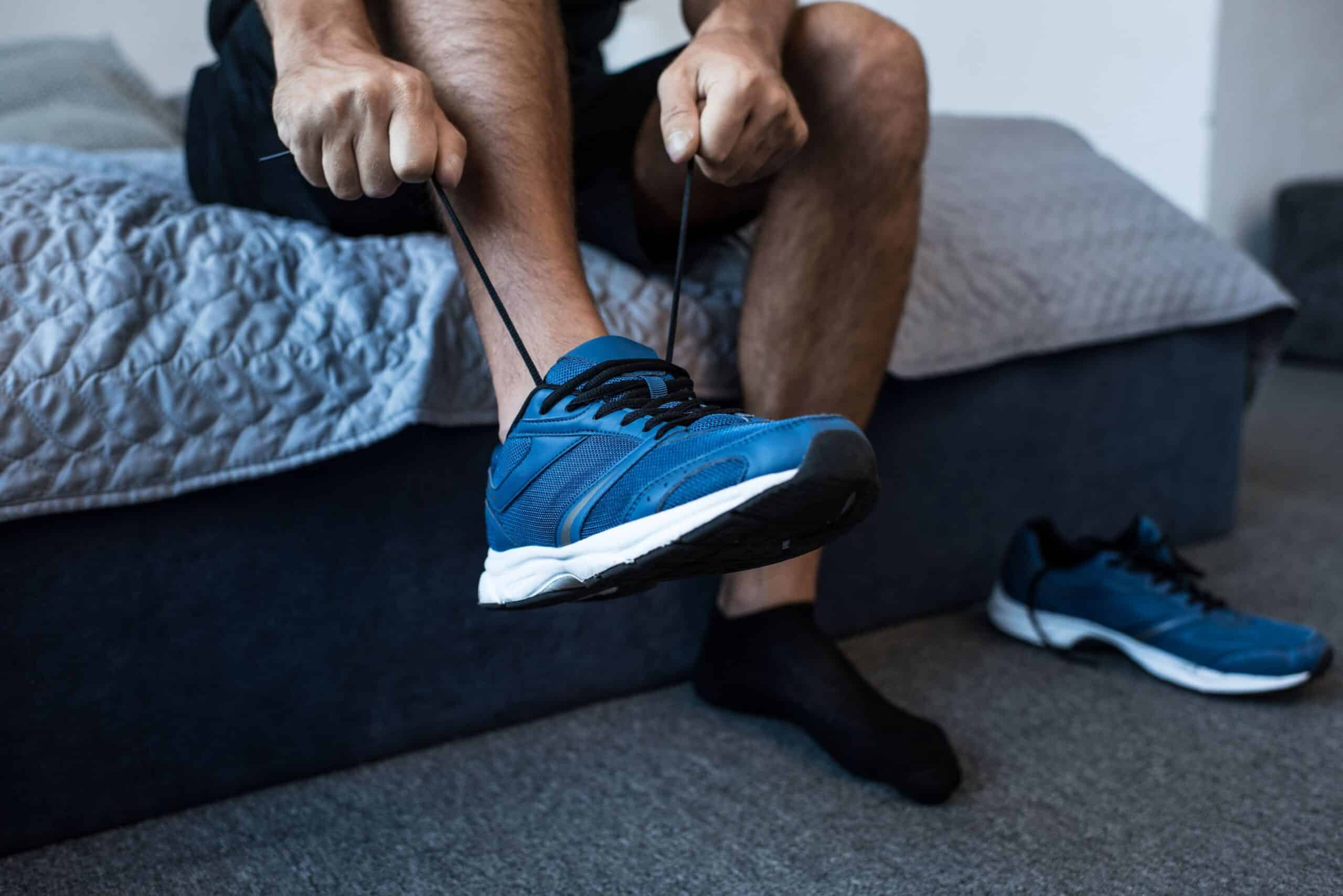 Gait training, image of a man sitting on the edge of a bed putting on blue sneakers.