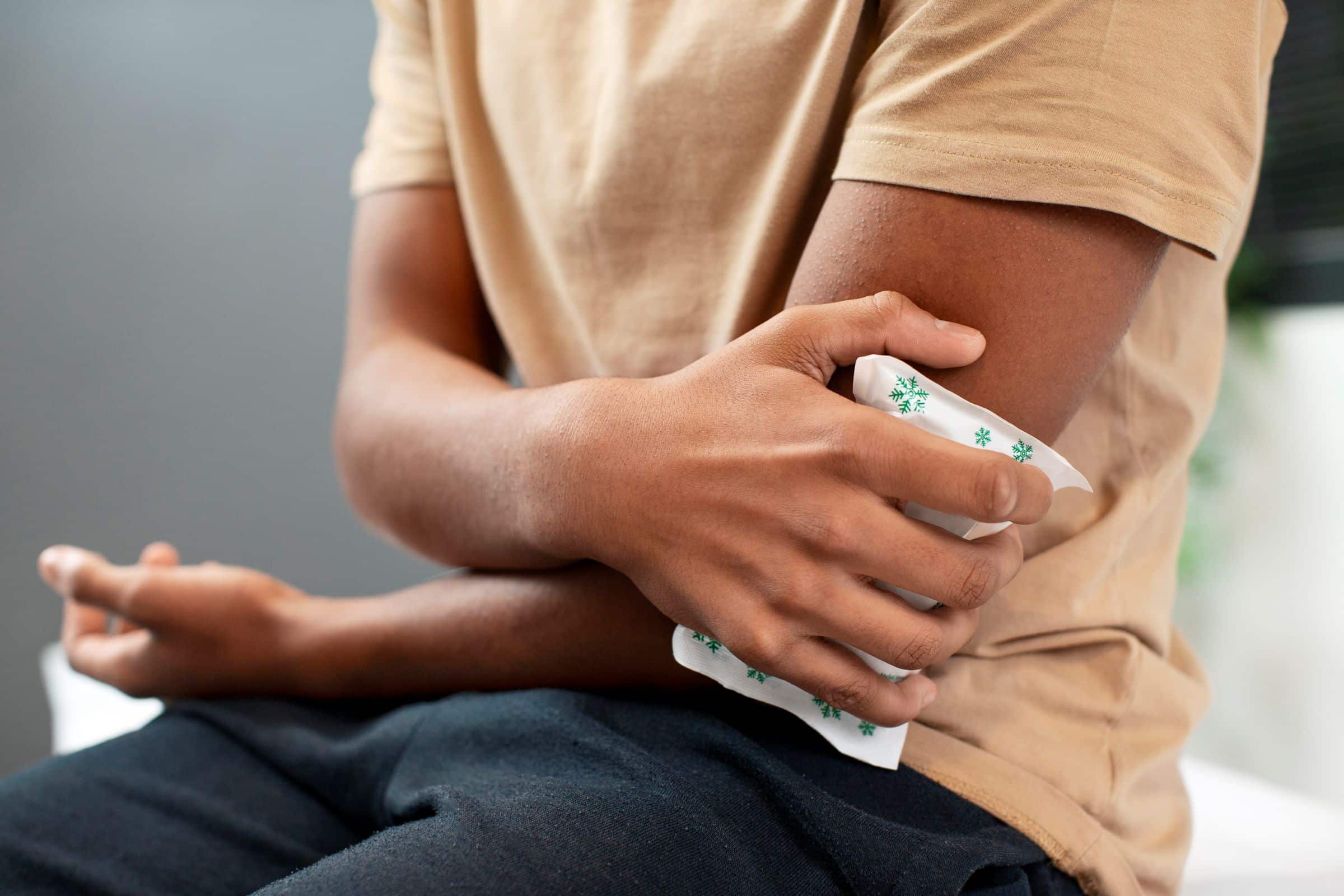 Stages of Inflammation, image of a man wearing a tan t-shirt and dark wash jeans sits and holds an ice pack on his left elbow.