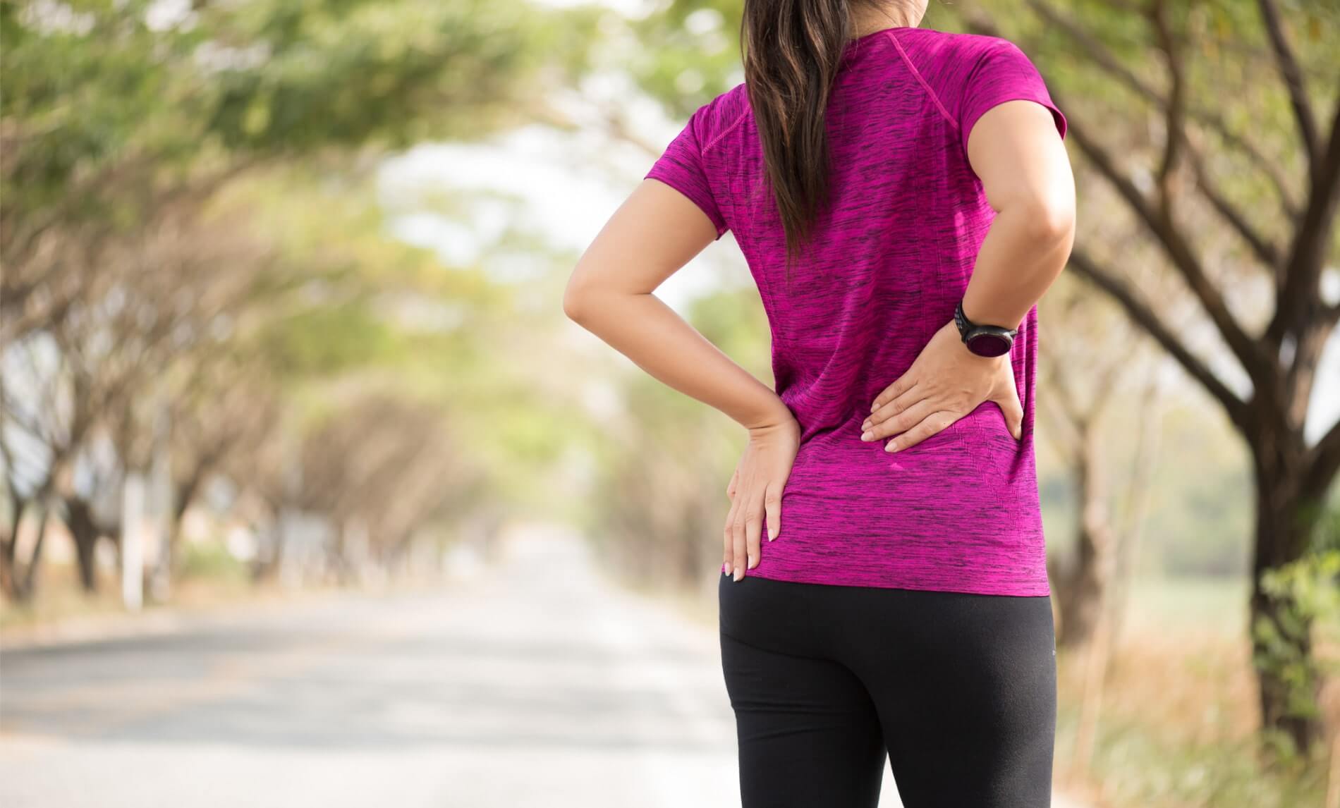 Lower back hurts when walking, image of a woman walking outside with her hands on her lower back.
